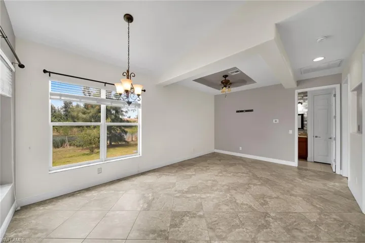 Unfurnished dining area with baseboards, ceiling fan, a chandelier, beamed ceiling, and light stone finish floors