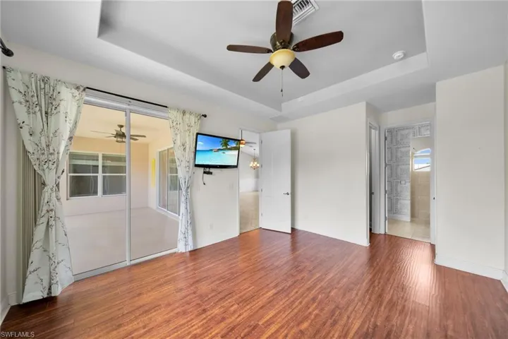 Empty room with a tray ceiling, a ceiling fan, wood finished floors, and baseboards