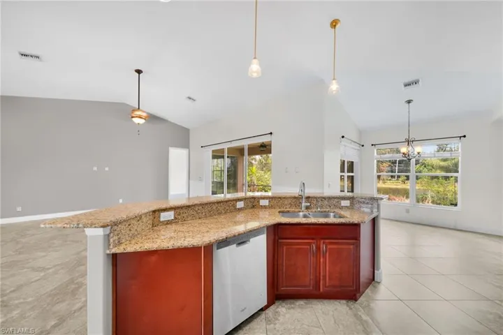 Kitchen featuring a sink, dishwasher, lofted ceiling, reddish brown cabinets, and a chandelier