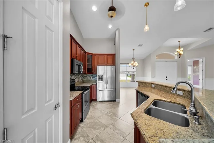 Kitchen featuring stainless steel appliances, a chandelier, a sink, pendant lighting, and backsplash