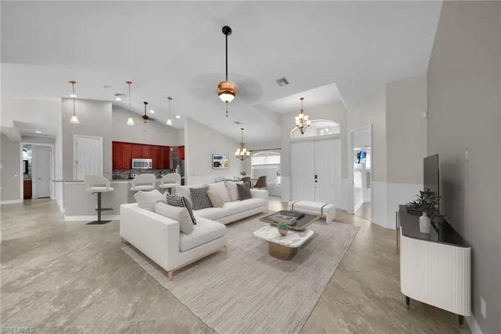 Living room with a chandelier, high vaulted ceiling, ceiling fan, and baseboards