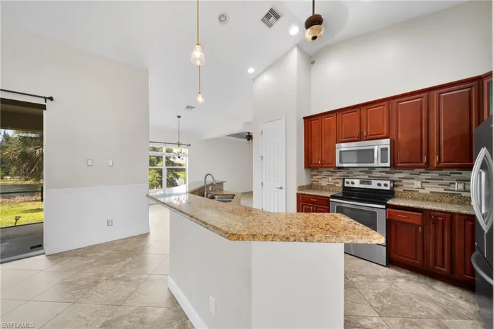 Kitchen featuring stainless steel appliances, a sink, backsplash, light tile patterned floors, and hanging light fixtures