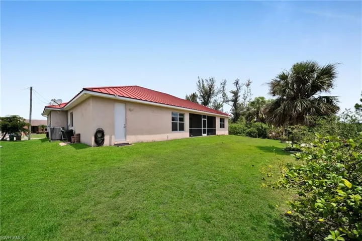 Rear view of house with stucco siding, metal roof, a lawn, and a standing seam roof