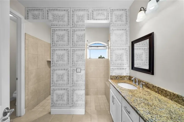 Bathroom with toilet, vanity, tile patterned flooring, walk in shower, and tile walls