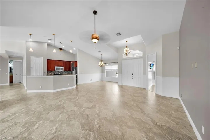 Unfurnished living room featuring a chandelier, high vaulted ceiling, ceiling fan, and baseboards