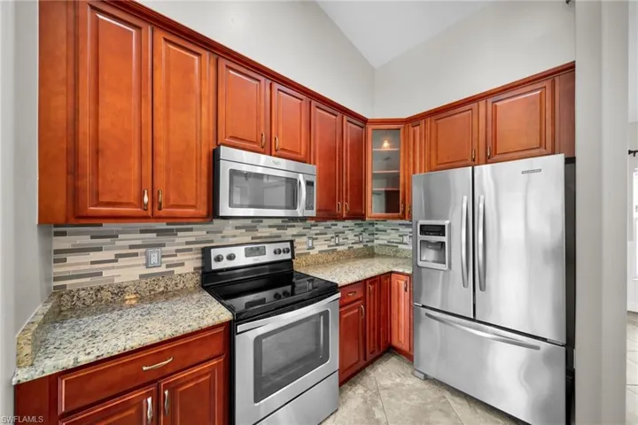 Kitchen with stainless steel appliances, tasteful backsplash, lofted ceiling, glass insert cabinets, and light stone counters