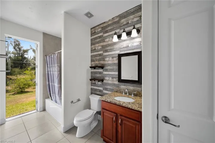 Bathroom with an accent wall, tile patterned floors, vanity, toilet, and shower / bath combo