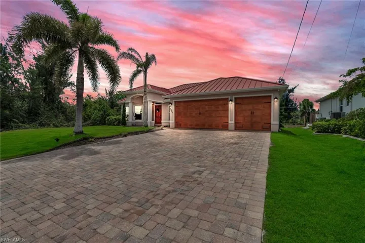 View of front facade with decorative driveway, a standing seam roof, an attached garage, and a front yard