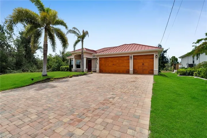 View of front of home featuring a standing seam roof, decorative driveway, an attached garage, a front lawn, and metal roof