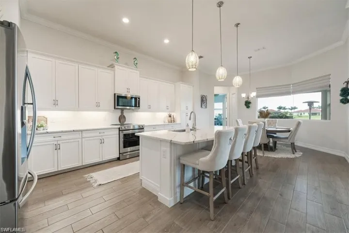 White cabinetry, stainless steel appliances, wood-finish flooring, recessed lighting, and a kitchen island with pendant lighting