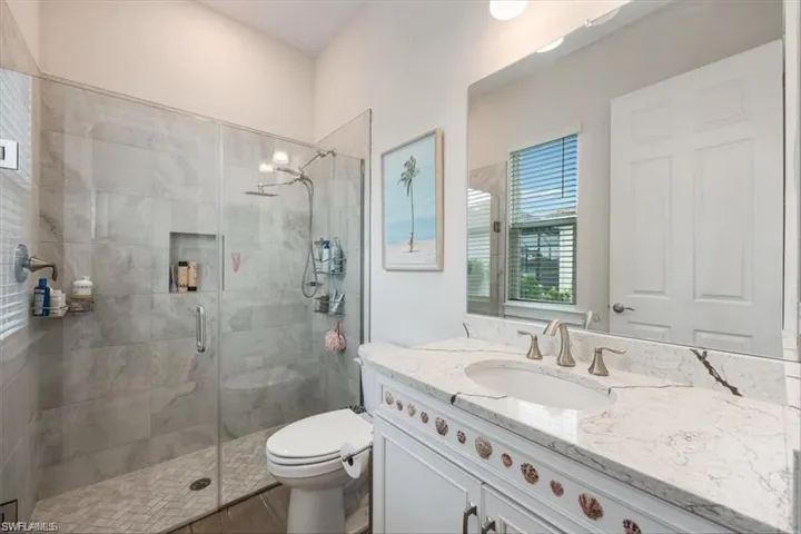 Spa-inspired primary bathroom featuring a frameless glass-enclosed walk-in shower with stone tile surround, dual vanity with marble countertop and brushed nickel fixtures, and a separate toilet compartment