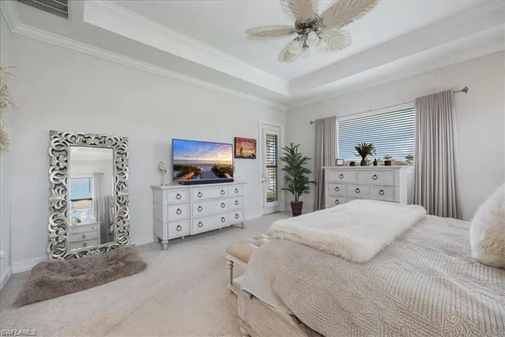 Tray ceiling with crown molding, ceiling fan, carpeted flooring, large window with blinds and drapery, and a glass-paneled door