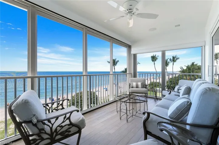 Sunroom / solarium with view of water and beach, plenty of natural light, wood finished floors, and floor to ceiling windows