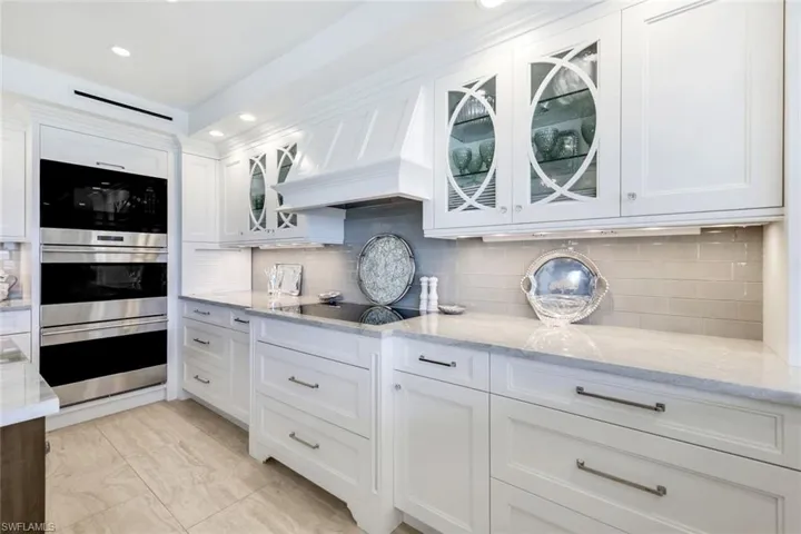 Kitchen with white cabinets, backsplash, light stone counters, custom range hood, and stainless steel double oven