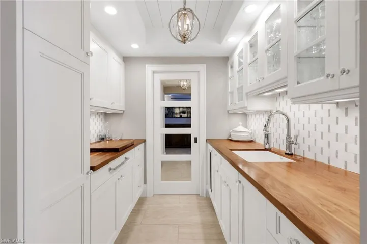 Kitchen with butcher block counters, white cabinets, hanging light fixtures, decorative backsplash, and glass insert cabinets