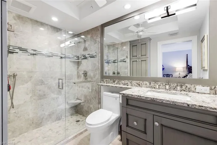 Ensuite bathroom featuring a shower stall, vanity, ceiling fan, and a tray ceiling