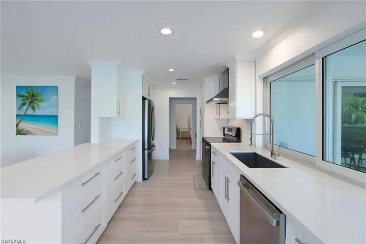 Kitchen with appliances with stainless steel finishes, white cabinets, light stone counters, a peninsula, and recessed lighting