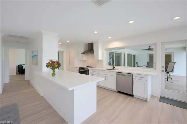 Kitchen featuring white cabinets, a peninsula, appliances with stainless steel finishes, wall chimney exhaust hood, and recessed lighting