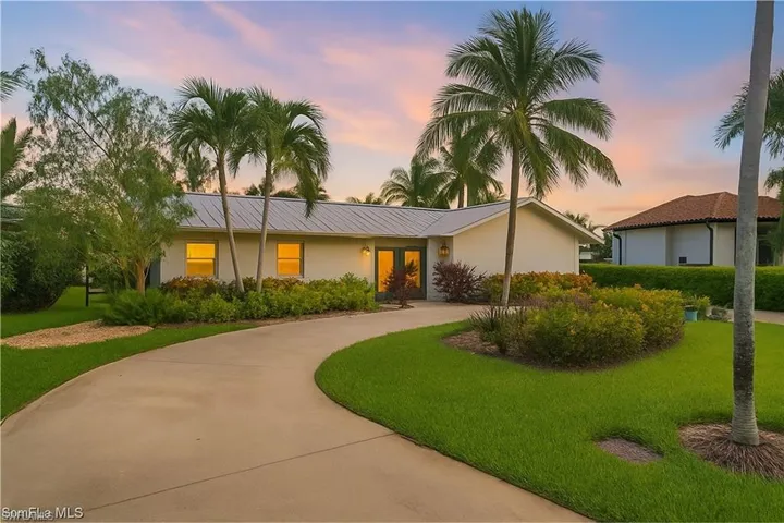 View of front facade featuring a front lawn, curved driveway, a metal roof, and stucco siding