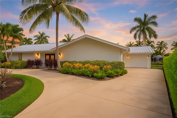 View of front facade featuring curved driveway, a metal roof, and stucco siding