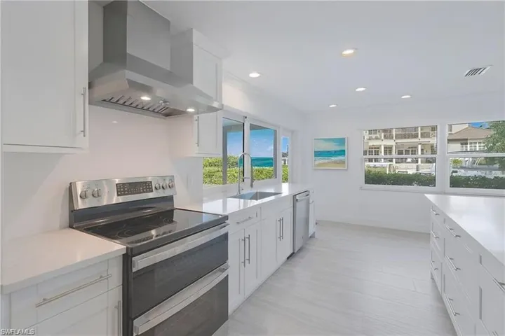 Kitchen with appliances with stainless steel finishes, white cabinets, wall chimney exhaust hood, recessed lighting, and light stone counters
