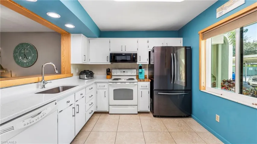 Kitchen with white appliances, white cabinetry, light tile patterned floors.