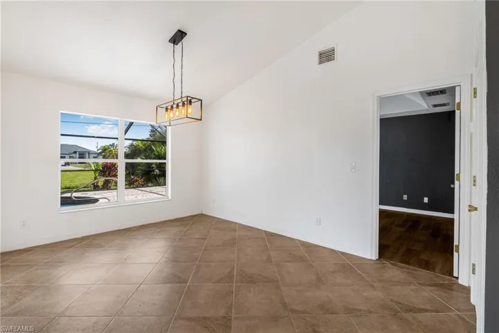Unfurnished dining area featuring an inviting chandelier, vaulted ceiling, and tile patterned floors