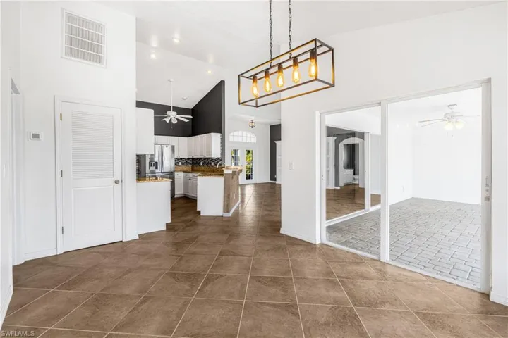 Kitchen with white cabinets, stainless steel fridge with ice dispenser, dark tile patterned floors, and high vaulted ceiling