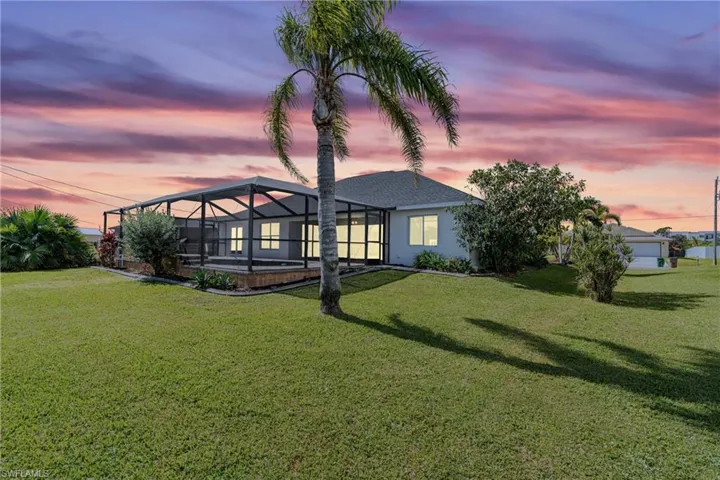 Back house at dusk with a lawn, a lanai, and a swimming pool