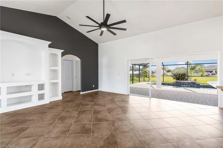 Unfurnished living room featuring high vaulted ceiling, built in features, tile patterned flooring, and ceiling fan