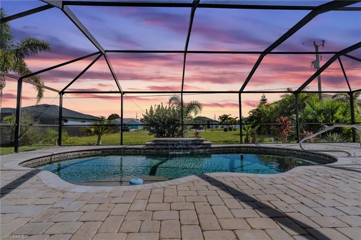 Pool at dusk featuring a lanai, a patio, and pool water feature