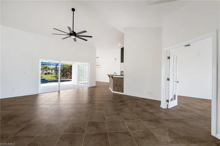 Unfurnished living room with high vaulted ceiling, dark tile patterned flooring, and ceiling fan