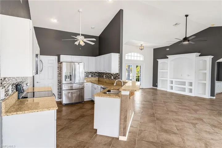 Kitchen with stainless steel appliances, light stone counters, white cabinets, kitchen peninsula, and high vaulted ceiling
