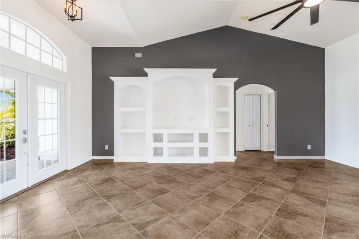 Unfurnished living room with built in features, french doors, dark tile patterned floors, vaulted ceiling, and ceiling fan with notable chandelier