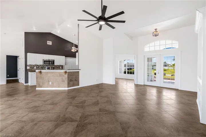 Unfurnished living room featuring french doors, high vaulted ceiling, ceiling fan, and dark tile patterned flooring