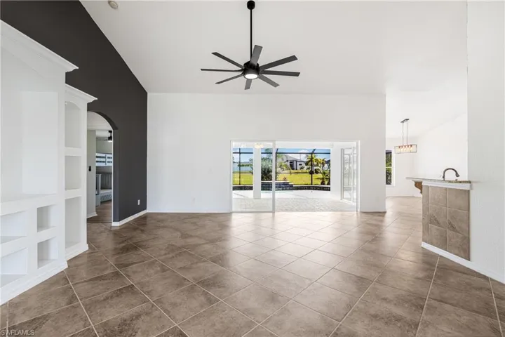 Unfurnished living room featuring built in shelves, ceiling fan, dark tile patterned floors, and vaulted ceiling