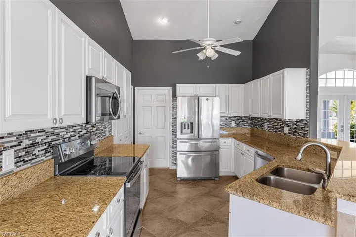 Kitchen featuring stainless steel appliances, sink, high vaulted ceiling, backsplash, and white cabinetry