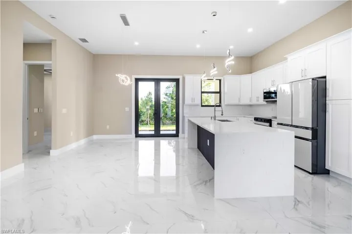Kitchen featuring freestanding refrigerator, light stone countertops, white cabinetry, french doors, and hanging light fixtures
