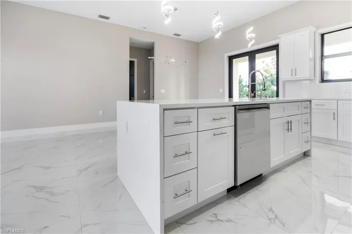 Kitchen with a kitchen island with sink, dishwasher, white cabinetry, light stone counters, and decorative light fixtures