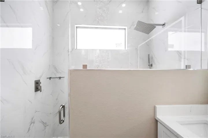 Full bath with a marble finish shower, vanity, and healthy amount of natural light