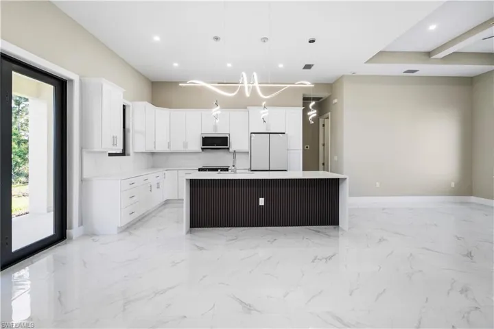 Kitchen featuring an island with sink, freestanding refrigerator, decorative light fixtures, white cabinets, and light stone counters