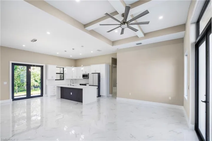Kitchen with open floor plan, french doors, a center island with sink, light marble finish flooring, and beam ceiling