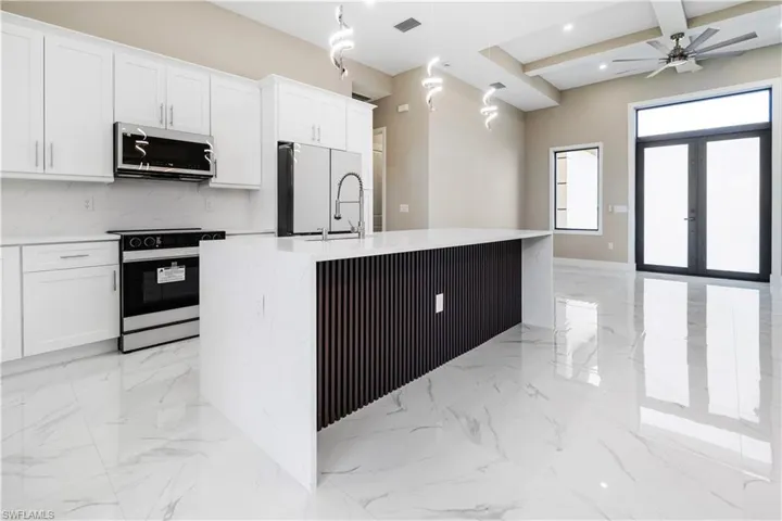 Kitchen featuring electric stove, stainless steel microwave, a kitchen island with sink, white cabinetry, and light stone counters