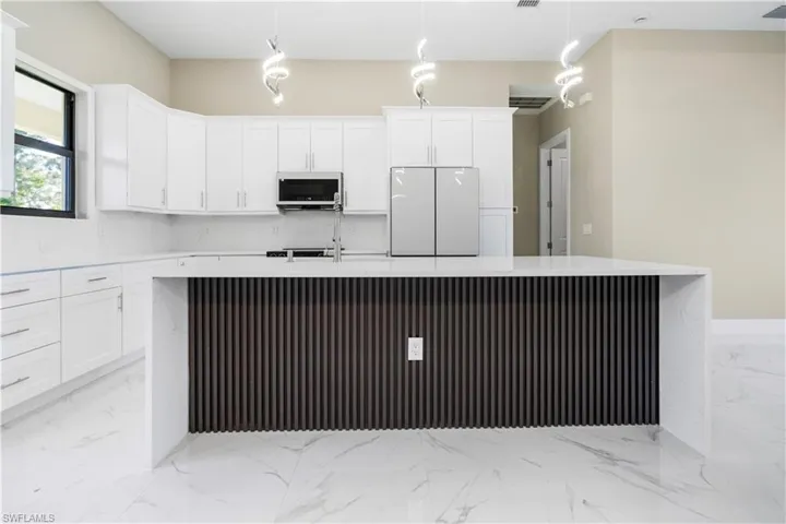 Kitchen with a kitchen island with sink, freestanding refrigerator, white cabinetry, and light stone counters