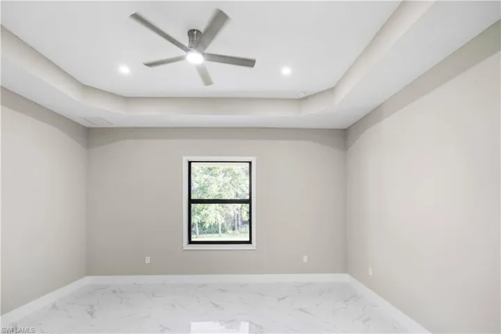 Spare room featuring a tray ceiling, light marble finish flooring, ceiling fan, and recessed lighting