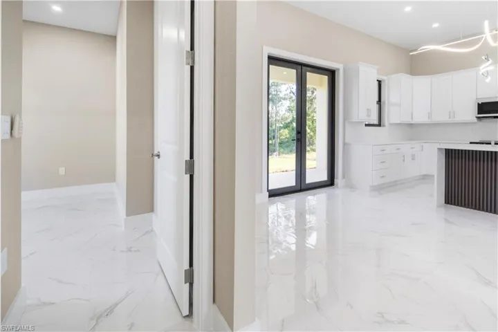 Kitchen with french doors, light marble finish floors, white cabinets, white microwave, and pendant lighting