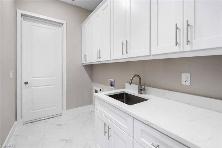 Laundry area featuring hookup for a washing machine, light marble finish floors, and cabinet space