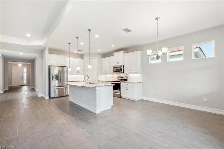 Kitchen with pendant lighting, light hardwood / wood-style floors, white cabinets, and appliances with stainless steel finishes