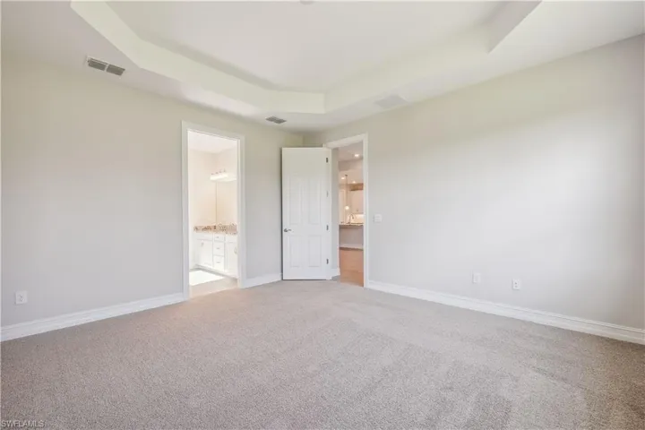 Unfurnished bedroom featuring connected bathroom, carpet, and a raised ceiling