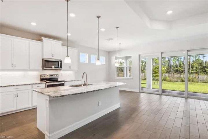Kitchen with light stone counters, white cabinetry, sink, and stainless steel appliances